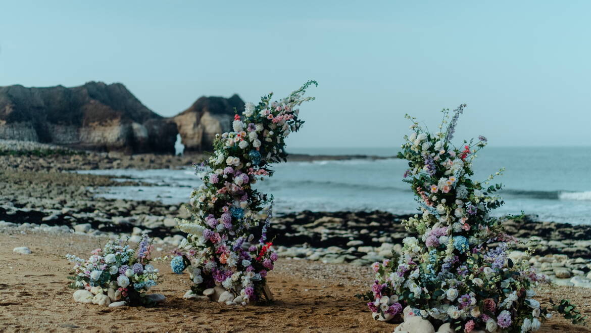 Romantic seaside elopement picnic with soft pastel florals, flowing linens, and candles set against coastal Yorkshire cliffs