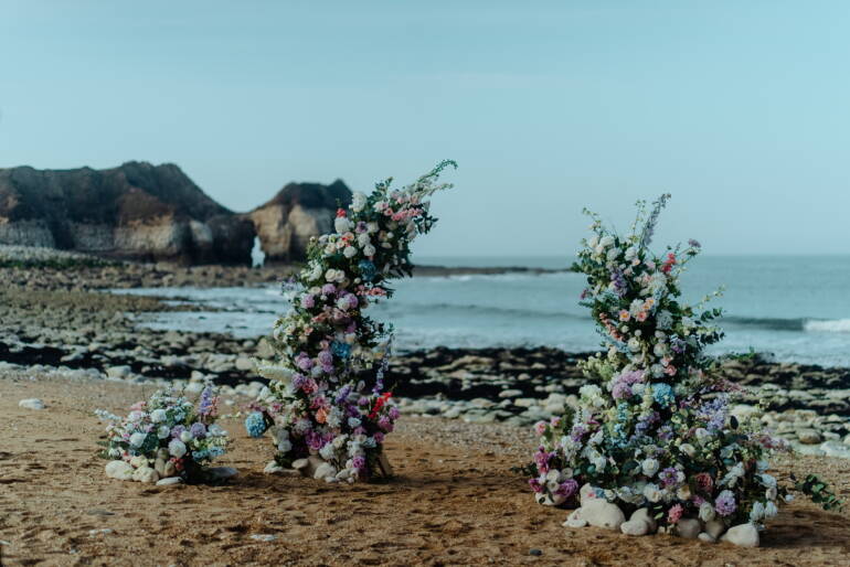 Romantic seaside elopement picnic with soft pastel florals, flowing linens, and candles set against coastal Yorkshire cliffs
