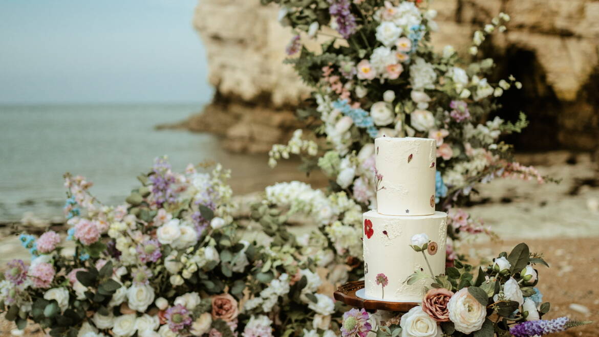 Romantic seaside elopement picnic with soft pastel florals, flowing linens, and candles set against coastal Yorkshire cliffs