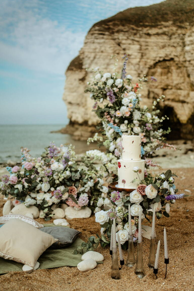 Romantic seaside elopement picnic with soft pastel florals, flowing linens, and candles set against coastal Yorkshire cliffs
