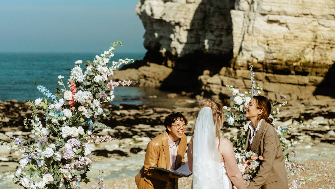 Romantic seaside elopement picnic with soft pastel florals, flowing linens, and candles set against coastal Yorkshire cliffs