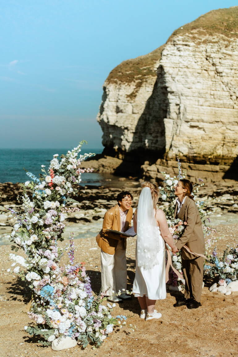 Romantic seaside elopement picnic with soft pastel florals, flowing linens, and candles set against coastal Yorkshire cliffs